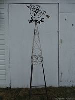 Full-length front view of tall metal obelisk with weathervane against a white wall