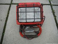 Front view showing the red halogen light with black metal protective cage and the red base with foam grips.