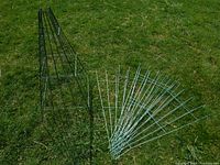 10 small green wire trellis panels arranged on the grass. One panel is standing upright, others spread flat showing the wire framed grid pattern and tapered design.