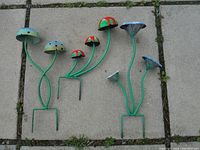 Three metal garden mushroom stakes laid on stone tiles showing bright colors and size reference.