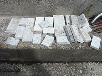 22 marble rectangular and square trophy bases laid out on a stone surface, showing varying sizes and white to off-white coloring with grey veining.