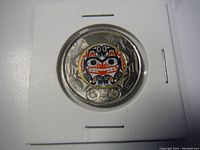 Close-up photo of the twoonie coin, highlighting the colored indigenous design by Bill Reid.