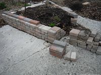 Stacked rectangular and square pavers used as raised garden bed edging on concrete ground