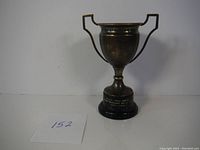 Full view of the vintage silver plated trophy with two handles and mounted on a round black base.