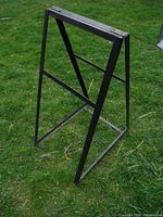 Full angled view of the metal sandwich sign frame on grass background, showing structure and condition.