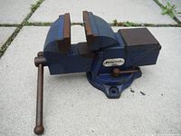 Blue swivel bench vice resting on a tiled surface showing the operational handle and jaw interior.