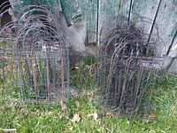 Two stacks of black wire fence panels with arched tops and decorative patterns, standing on grass in front of a weathered wooden structure.