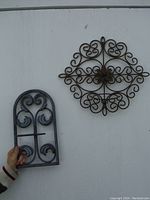 Close-up of vertical plant holder held by hand against wall showing decorative scroll design and size comparison.