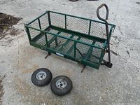 Side view of the Yardworks garden cart with two flat tires removed placed on the ground in front of it. Green painted metal with mesh sides visible, fold-down sides are secured upright.