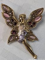 Angel-shaped pin brooch with decorative pink and purple stones on wings and body, gold-tone metal base