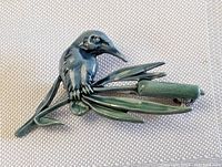 Close-up photo of the enamel bird pin brooch showing the bird perched on a branch with leaves, highlighting the detailed texture and green enamel.