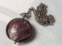 Close-up of round art glass pendant with metallic pink and black swirls attached to the sterling silver chain