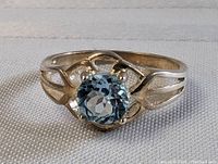 Front view of sterling silver ring with blue topaz gemstone set in prongs, showing intricate band design.