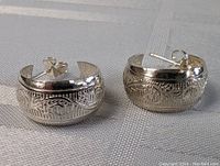 Pair of sterling silver half-hoop earrings showing carved detailed motifs and overall shape