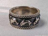 Close-up photo showing detailed raised dolphin designs on the wide sterling silver band ring.