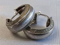 Pair of sterling silver hoop earrings with a frosted matte finish and textured encrusted detailing along the outer edge