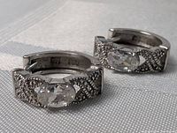 Close-up of one sterling silver hoop earring with an oval clear stone and textured encrusted design on the band.