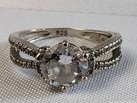 Front angle showing large round clear faceted center stone and split band with small dark stones