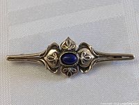 Sterling silver Art Nouveau pin brooch with central oval lapis lazuli cabochon, showing detailed curvilinear design on sides and floral motifs.