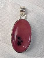 Close-up view of the oval pink rhodonite gemstone set in sterling silver pendant showing the polished smooth surface and black natural inclusions.