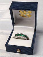 Full view of the sterling silver ring with green and clear stones inside a blue and white jewelry box.