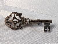 Front side view of the vintage sterling silver skeleton key brooch pin showing intricate openwork design on the bow and smooth shaft with decorative rings.