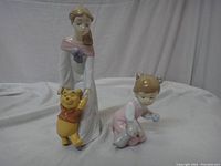Front view of both figurines showing woman in white dress holding Winnie the Pooh and child kneeling in pink outfit