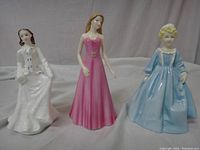 Front view of three porcelain figurines with detailed dresses and painted faces.