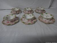 Six antique fruit cups with matching saucers arranged in two rows on white background. Floral designs in pink and green with scalloped edges visible.