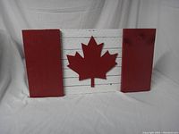 Front view of the painted wood Canada flag sign showing the red maple leaf and red/white paint on reclaimed wood slats.