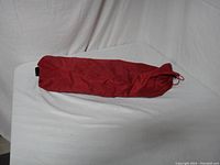 Red fabric bag containing tent components on white surface.