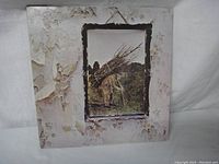 Front cover of Led Zeppelin IV album depicting man carrying sticks in a worn frame style.