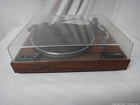 Front angle view of Micro Seiki DD-24 turntable with dust cover closed and wood veneer plinth