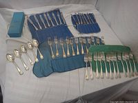 Full set of flatware displayed on cloths showing quantity, different types of pieces laid out.