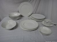 Full set of white Johnson Bros Athena dinnerware pieces arranged in groups on a plain white draped background: stack of bowls, plates, platters, saucers, and gravy boat.