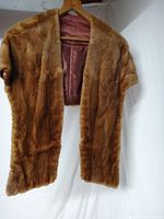 Front view of the vintage mink fur shawl hanging on a wooden hanger showing the brown fur and inner pink satin lining.