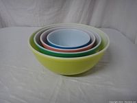 Nested arrangement of four PYREX mixing bowls showing yellow, green, pink, and blue colors.