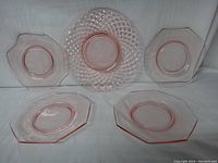Five pink glass plates displayed: four octagon-shaped plates and one larger round weave-style plate.