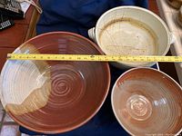 Top view of three stoneware bowls with measuring tape showing approximately 14 inches diameter for the large rust and beige bowl, smaller rust/beige bowl, and large beige bowl with handles.