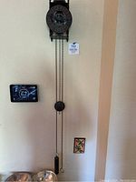 Full view of cast iron skeleton wall clock hanging on wall showing dial, weight and pendulum down to floor level.