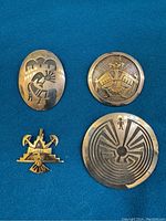 All four pieces displayed on blue background: two circular sterling pins, one oval sterling pin, one gold pendant