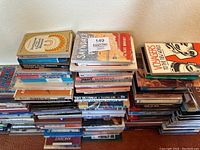Stacks of various Native American history and culture books arranged in piles on the floor, showing book spines and some front covers with diverse titles.