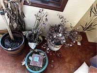 Wide view showing five clay planter pots with dried plants inside. Includes one turquoise pot with moss and auction tile, white pot with dry leafy branches, and dark brown textured pot with foil-wrapped plant stems.