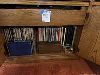 Wooden cabinet shelf containing upright vinyl LP records and two cassette carrying cases alongside a small stack of cassette tapes.
