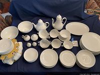 Overall layout of white porcelain dinnerware set including plates, bowls, cups, saucers, serving pieces