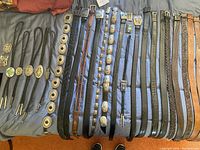 Overview of six braided cord bolo ties, multiple concho and inlaid stone belts, and plain leather belts laid flat