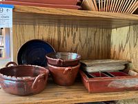 Shelf with large handled bowls, medium handled bowls, rectangular serving tray with compartments and a dark blue round plate.
