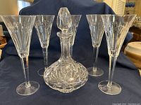 Five Waterford crystal toasting flutes and one crystal decanter with stopper displayed on a dark cloth.