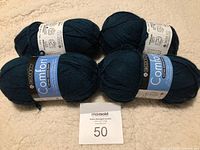 Four balls of dark blue Berroco Comfort yarn arranged on a soft beige blanket.
