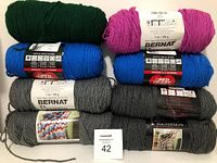 Eight balls of medium weight 4 yarn from Red Heart and Bernat in various colors including green, pink, blue, and shades of gray.